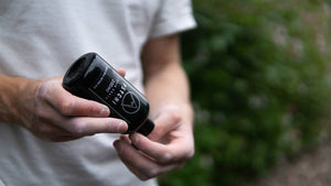 A climber opens a black bottle of psychi liquid chalk at rubicon crag in the peak district