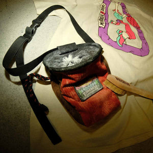 Burnt orange and brown corduroy climbing chalk bag sits on a bouldering crash mat next to a t-shirt and boulder brush.