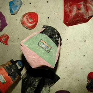 A light green and pink corduroy boulder bucker hanging from a rock climbing hold at Parthian Climbing Centre Manchester.