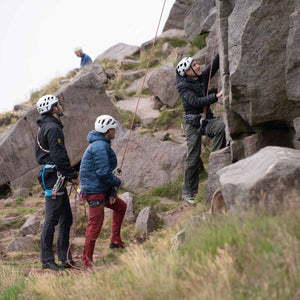 A group of climbers belay their friend as he ascends a rock face at Bamford Edge in the Peak District