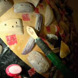 A stick with a rock climbing brush taped to the end reaches towards a hand hold on a climbing wall at Parthian Climbing Centre in Manchester.