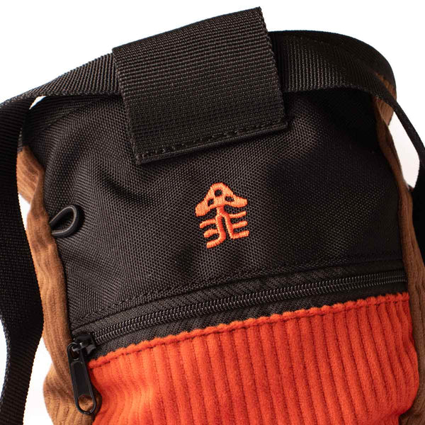 an orange embroidered hikerdelic logo sewn into a black panel on a rock climbing chalk bag