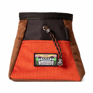 A burnt orange, brown and black corduroy bouldering bucket with drawstring closure and an elastic brush holder.