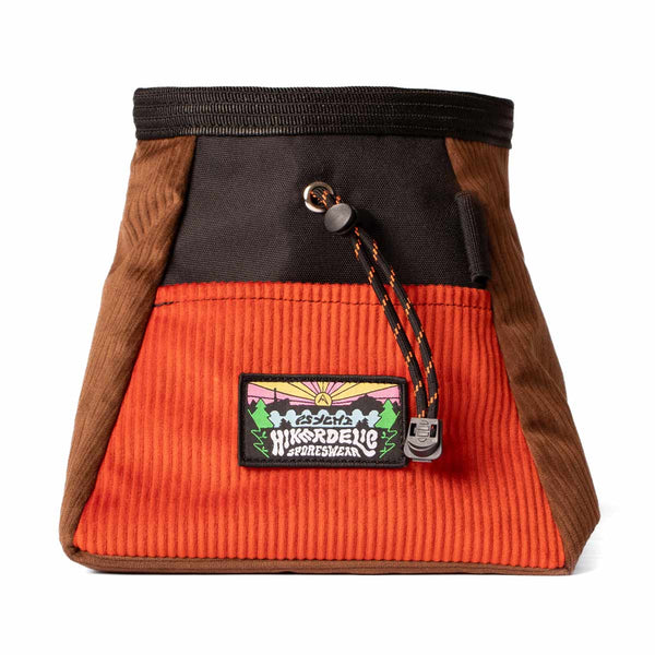 A burnt orange, brown and black corduroy bouldering bucket with drawstring closure and an elastic brush holder.