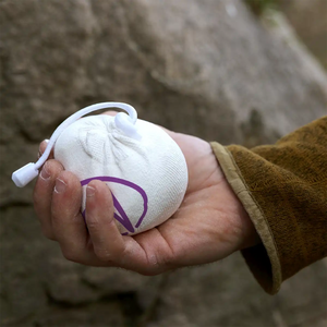 A climber holds a refillable cotton chalk ball in front of a boulder in the Peak District