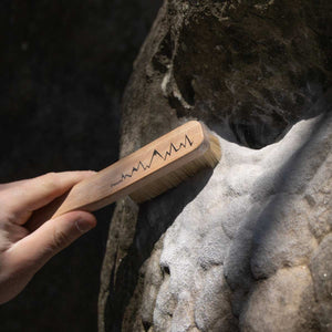 A boulderer in Fontainbleau, France cleaning a boulder with a wooden boar hair climnbing brush