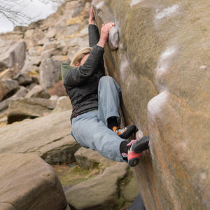 A climber clings to a large boulder. Both her feet are planted in a crack as she pulls herself to the top.