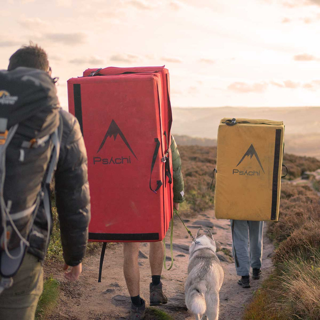 Climbers carrying red and yellow bouldering pads with a dog at Stanage Edge, Peak District.