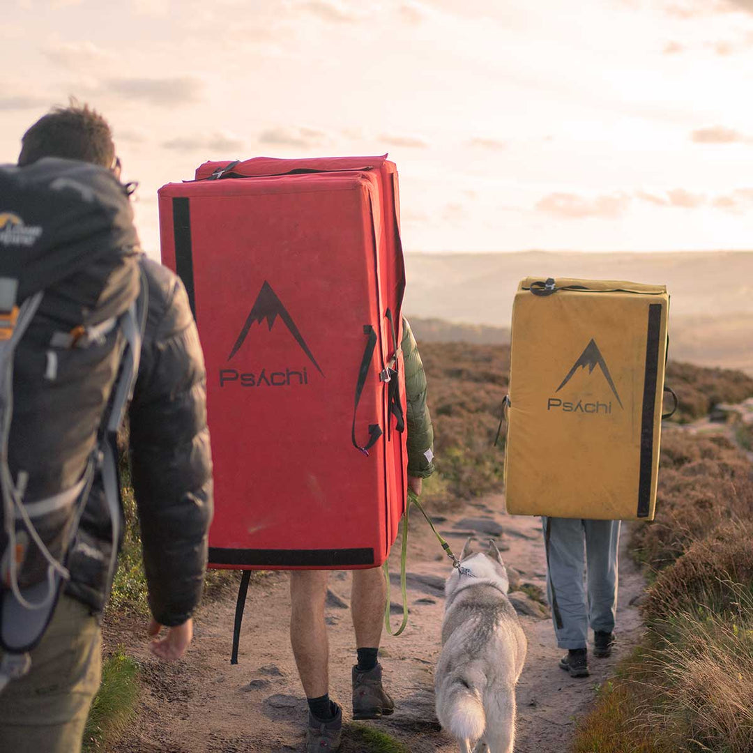 Climbers carrying red and yellow bouldering pads with a dog at Stanage Edge, Peak District.