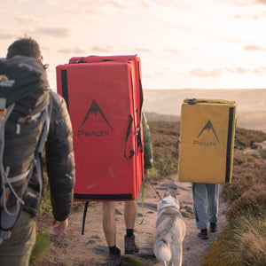 Climbers carrying red and yellow bouldering pads with a dog at Stanage Edge, Peak District.