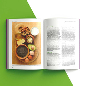 An open book spread showing a color photograph of healthy snack ingredients on a wooden board, with text columns on both pages, photographed against a green and white geometric background.