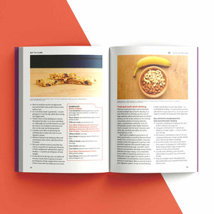 An open printed recipe book laid flat on a white background with large orange-red geometric shapes behind it. The spread shows two pages with food photos, headings, and blocks of text, including a banana and nuts in a bowl on one page and a baked good on the other.