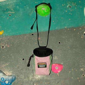 A muted pink and light green corduroy rock climbing chalk bag hanging from a climbing hold at Parthian Climbing Centre in Manchester.