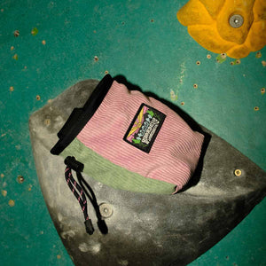 A muted pink and light green corduroy rock climbing chalk bag sitting on a bouldering hand hold at Parthian Climbing Center in Manchester.