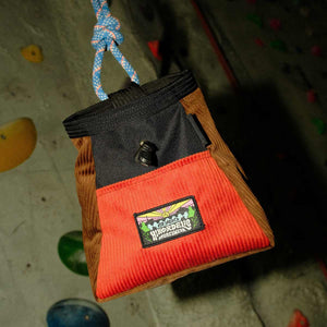 A burnt orange, brown and black corduroy bouldering bucket hanging from a climbing rope at Parthian Climbing Centre Manchester.