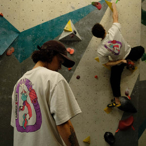 A climber in a hat looks down as a boulderer climbings a climbing wall at parthian climbing centre in manchester.