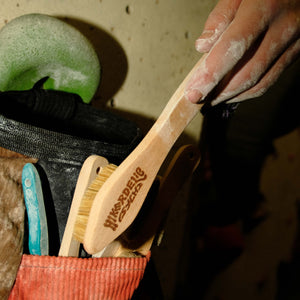 A boulderer putting a wooden bouldering brush into a pocket on their rock climbing chalk bucket.