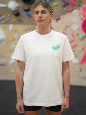 Unisex climbing apparel t-shirt modelled by female in front of a blurred indoor climbing wall.