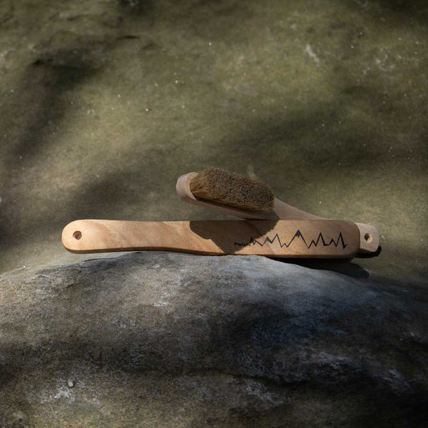 A smaller and larger wooden climbing brushes sit on a rock in Fontainbleau, France