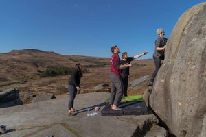 Group of climbers bouldering on a rocky outcrop with a moorland landscape in the background.