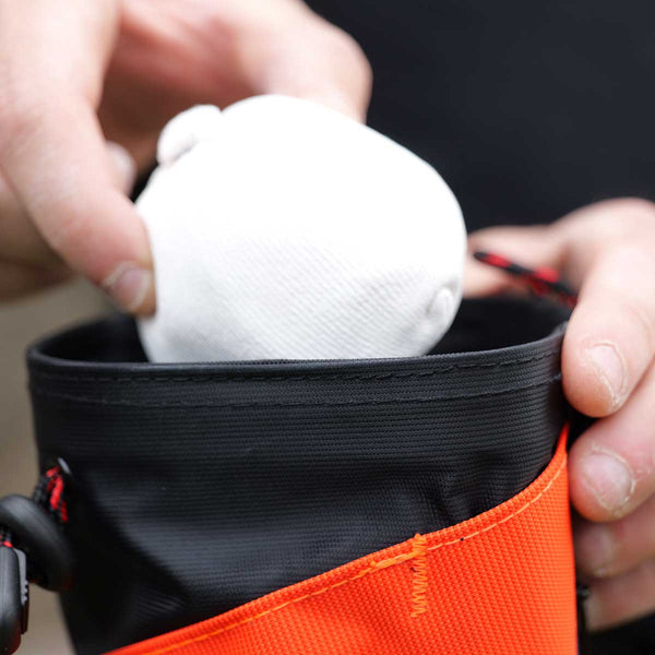 A climber putting a chalk ball into a psychi orange peak chalk bag