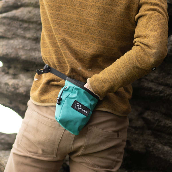 A climber dips his hand in a teal rock climbing chalk bag at burbage north in the Peak District