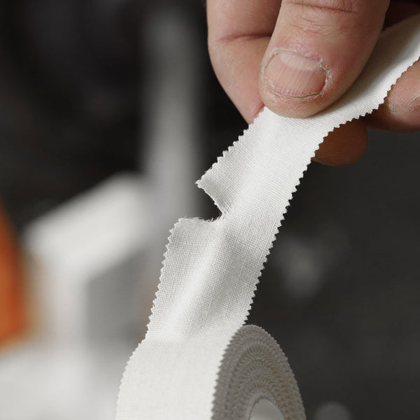 A climber tears off a section of white cotton finger tape at Depot climbing centre Manchester
