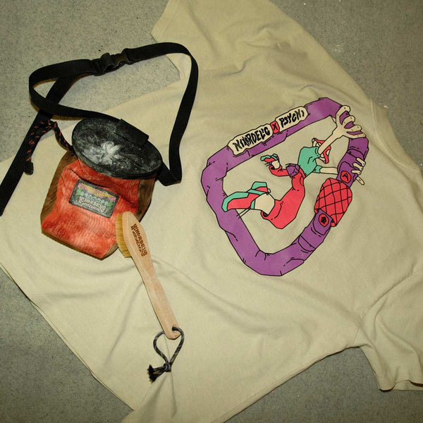 A rock climbing t-shirt, a chalky chalk bag and bouldering brush sit on a bouldering crash mat at Parthian Climbing Centre in Manchester.