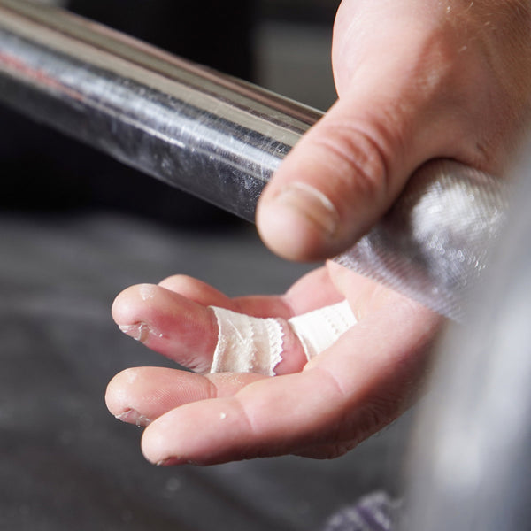 A weightlifter's hand with white finger tape strapping around his finger prepares to life a dumb bell.
