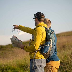 A mountain guide teaching a man to navigate with a map and compass on a hillside in the sun