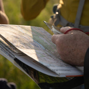 A map and compass being held by a mounatin guide and a person learning how to navigate