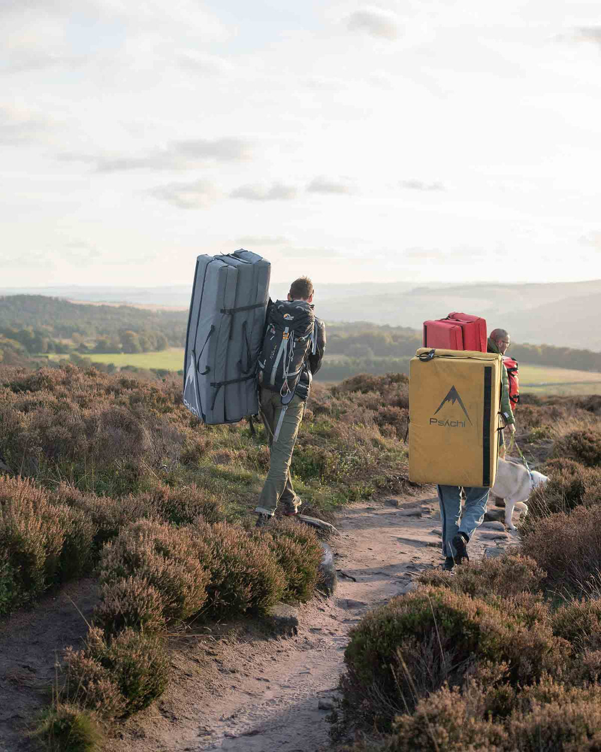 Boulderers walk along a path in the peak district carrying psychi bouldering pads