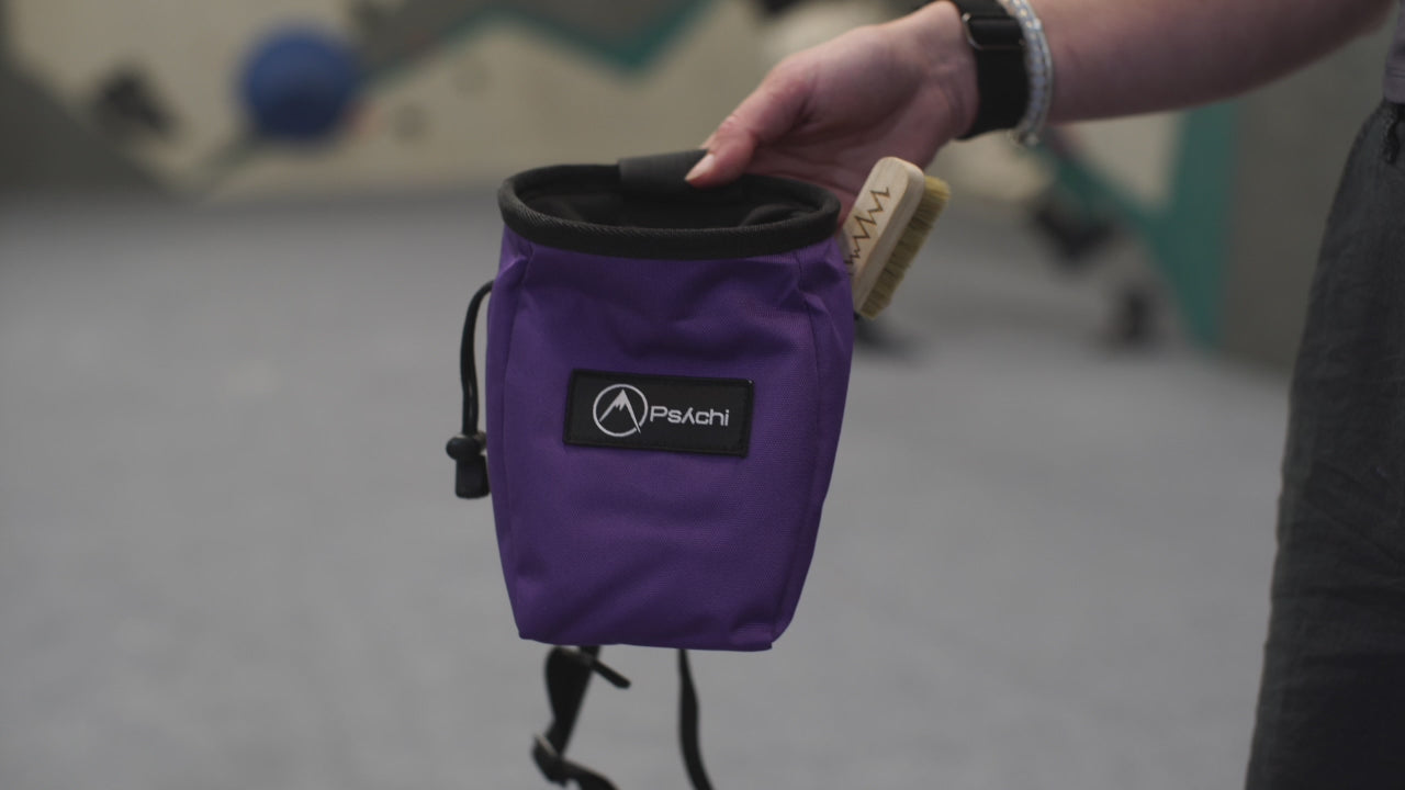 A climber using a purple chalk bag with zip pocket and black patch featuring 'PSYCHI' branding at a climbing centre in Manchester