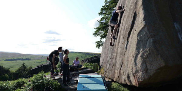 a group of climbers watch on as a boulderer ascends a rock face at Stanage Edge in the Peak District