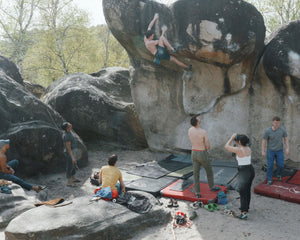 A woman taking a picture of a climber on a large boulder in Fontainebleau, France while others watch