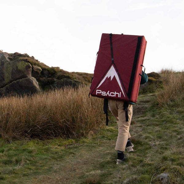 A boulderer carrying a bouldering crash mat walks up a steap path in Stanage, Peak District