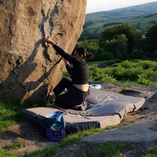 A female boulerer sit starting a problem on a bouldering pad in Stanage, Peak District