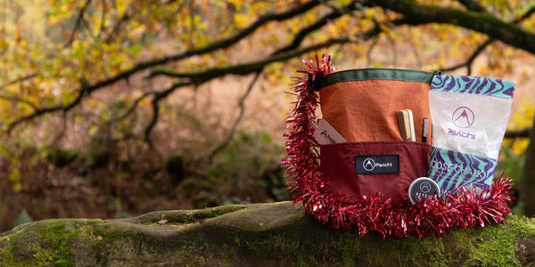 A sustainable bouldering bucket, climbing tape and chalk gift set wrapped with red christmas tinsel all sitting on a rock at Cratcliffe, Yokshire.
