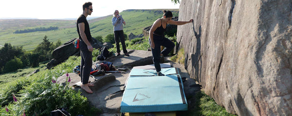 Climbers on a bouldering pad assess a boulder problem at stanage edge, Peak District
