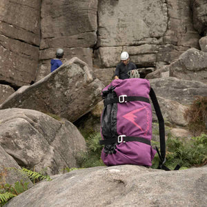 Purple rope bag with pink logo on a rocky landscape with people climbing in the background.