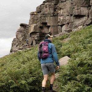 A climber carrying a purple rope bag approaches Stanage Edge crag in the peak district.